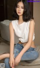 A woman sitting on top of a bed wearing a white shirt and jeans.